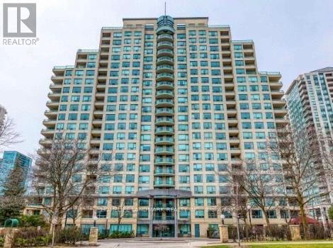 A tall building with many windows is surrounded by trees and other buildings.