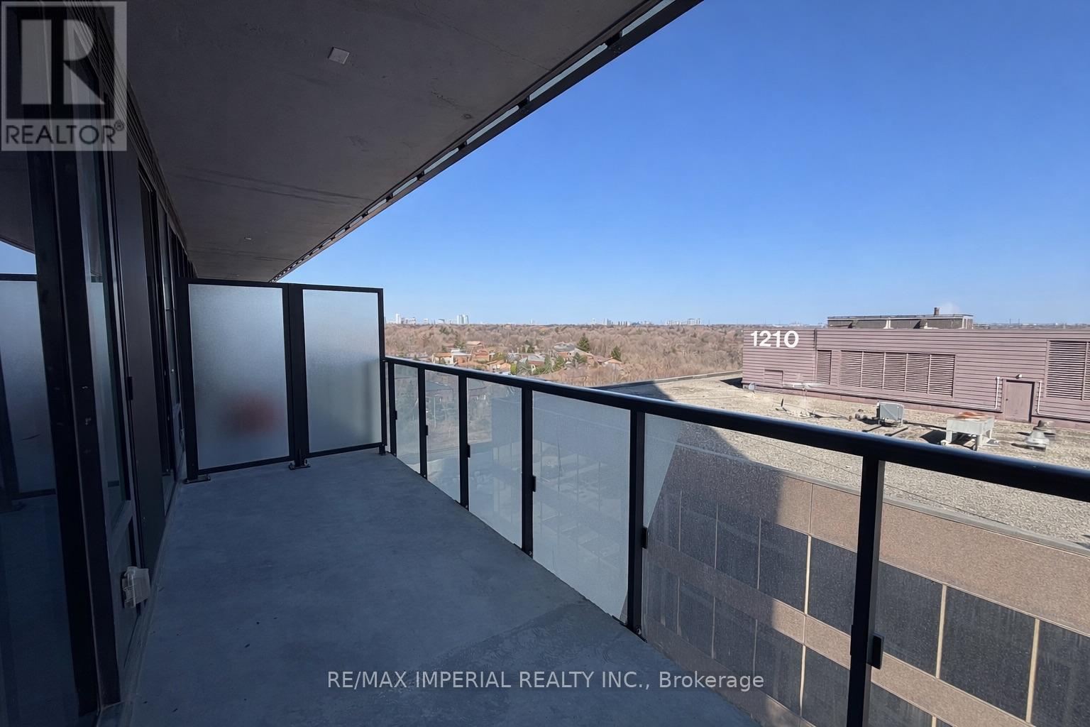 A balcony with a glass railing and a view of a building with the number 1210 on it.