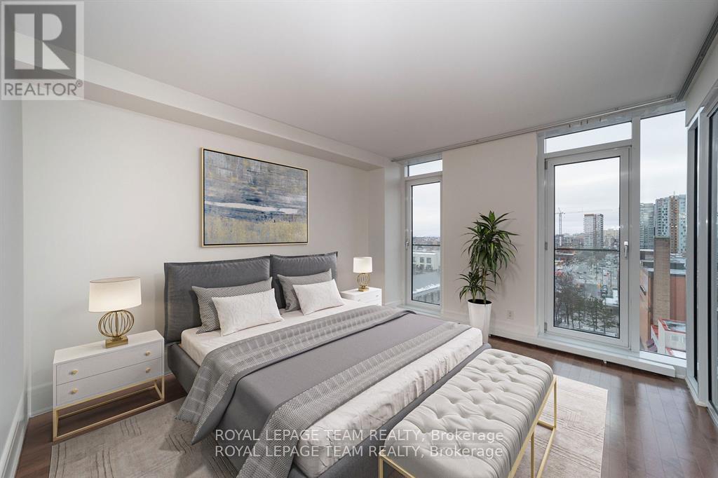 A bedroom with a large bed, a nightstand, and a window overlooking a cityscape.