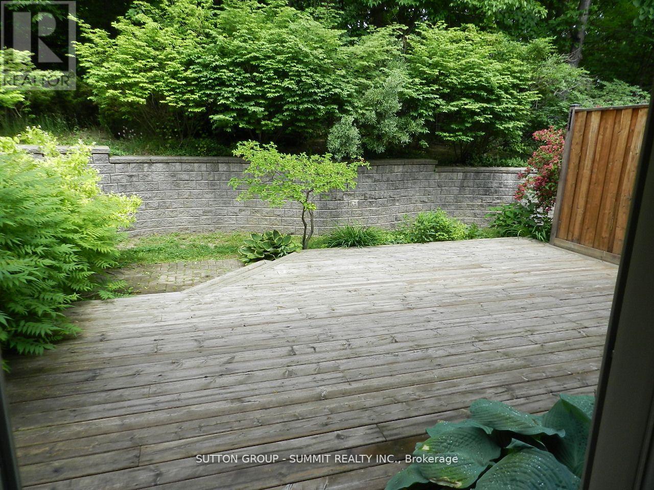 A wooden deck in a backyard with a wall and trees.