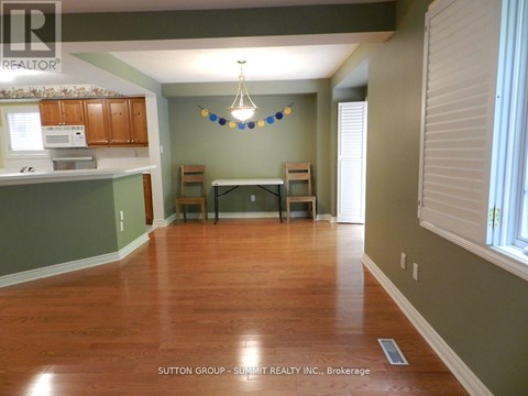 A room with wooden floors and a kitchen area with cabinets and a microwave.