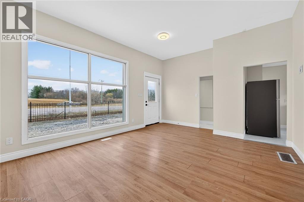 A spacious room with wood flooring and a large window overlooking a fenced area.