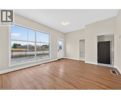 A spacious room with wood flooring and a large window overlooking a fenced area.
