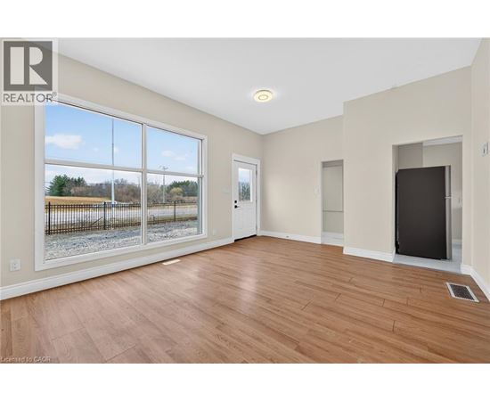 A spacious room with wood flooring and a large window overlooking a fenced area.