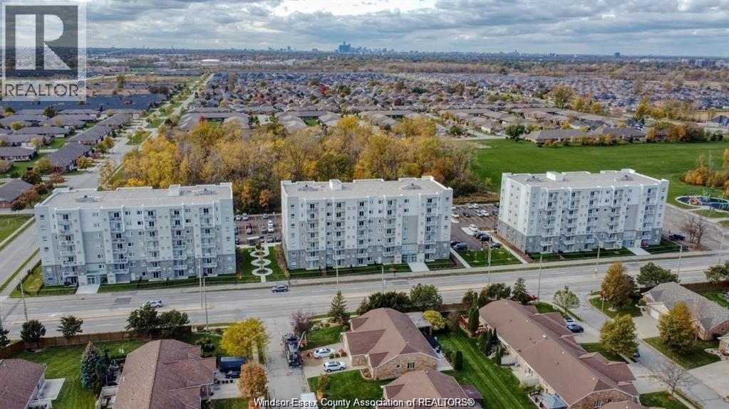 A real estate company logo is superimposed on an aerial view of a residential area with two apartment buildings and surrounding houses.