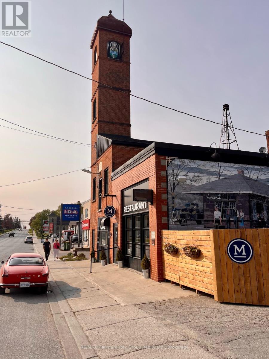 A red car is parked on the side of the street in front of a building with a clock tower.