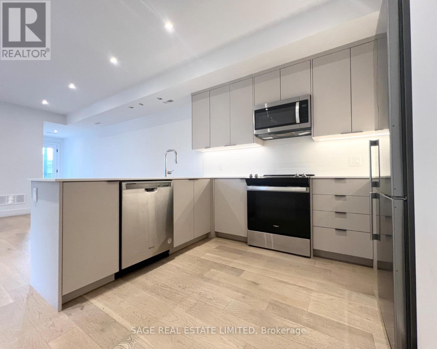A modern kitchen with stainless steel appliances and wooden flooring.