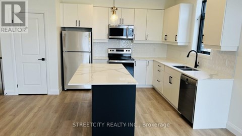 A kitchen with a refrigerator, microwave, oven, and sink.