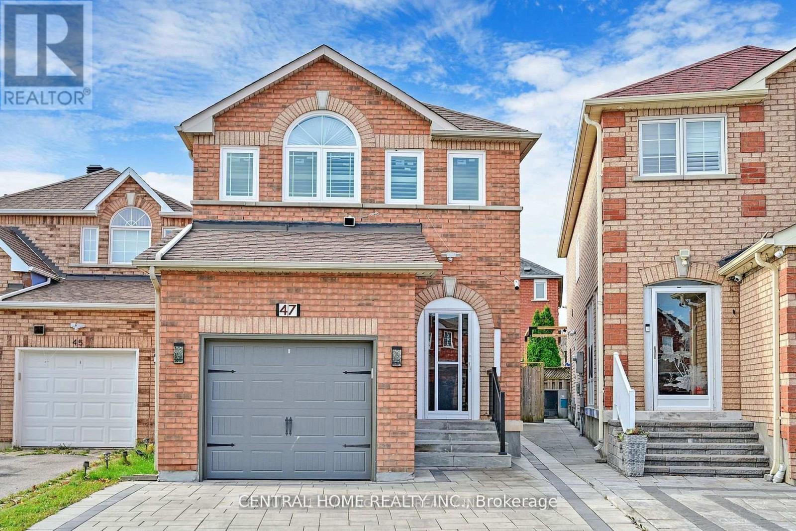 A red brick house with a grey garage door is for sale.