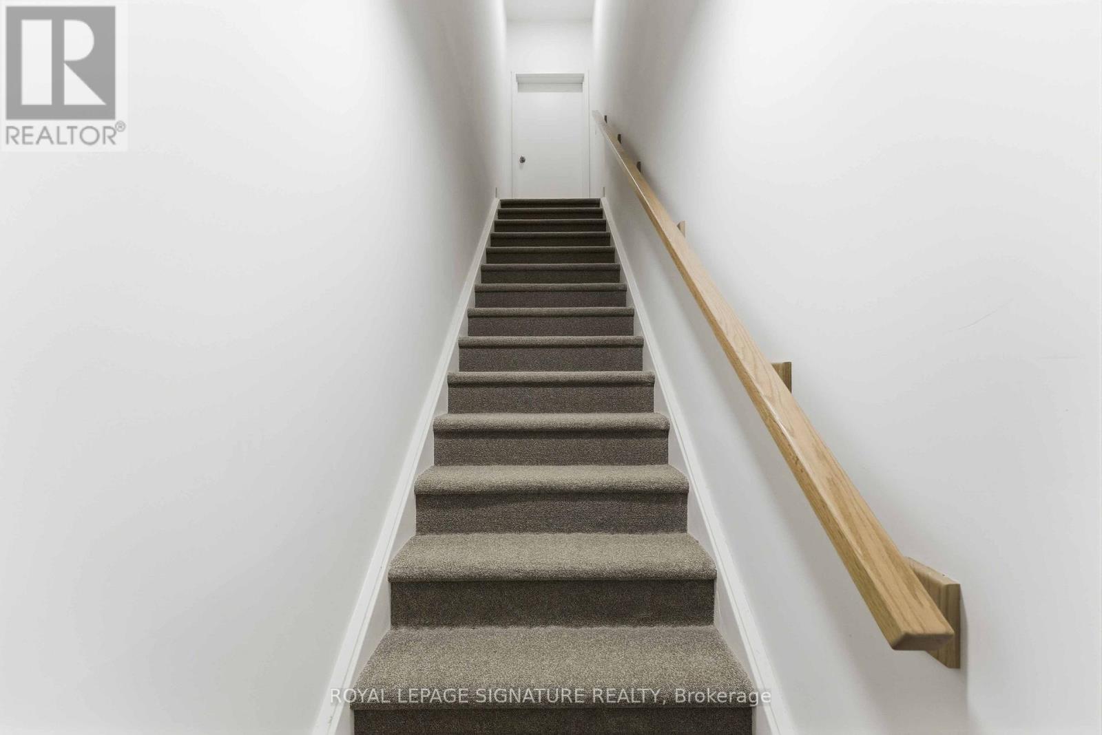 A staircase with a wooden handrail and carpeted steps.
