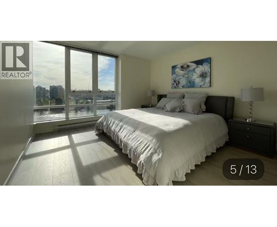 A bedroom with a large bed and a window overlooking a cityscape.