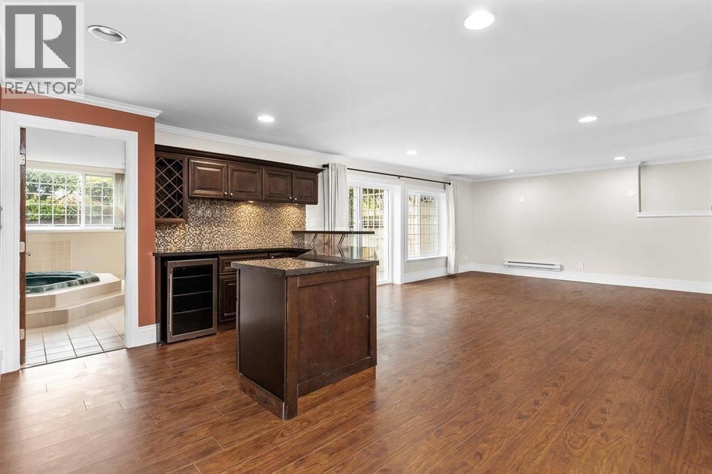 A large, empty room with a wooden floor and a kitchen area with a refrigerator, oven, and microwave.