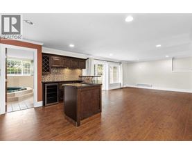 A large, empty room with a wooden floor and a kitchen area with a refrigerator, oven, and microwave.