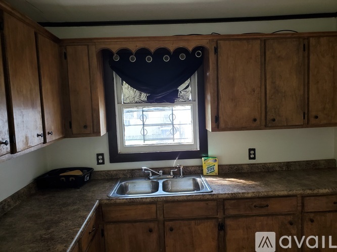 A kitchen with wooden cabinets and a window with a blue curtain.