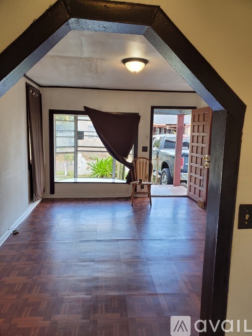 A hallway with a wooden floor and a large open door leading to a balcony.