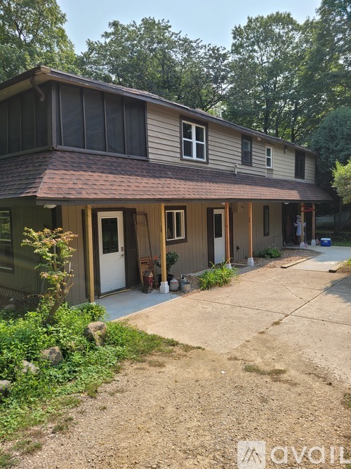 A house with a brown roof and a white door is surrounded by greenery.