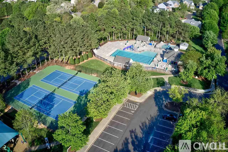 An aerial view of a tennis court surrounded by trees and a swimming pool.