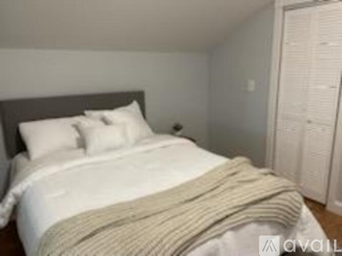 A bed with a white comforter and a striped blanket is in the image.