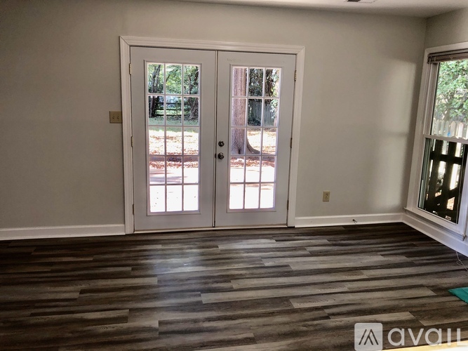 A room with a white door and a window with a view of trees.