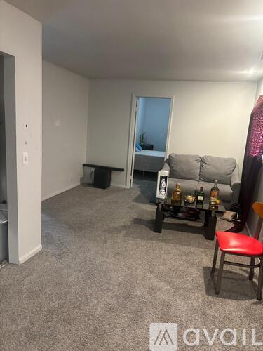 A living room with a grey couch, a red chair, and a small table with bottles on it.