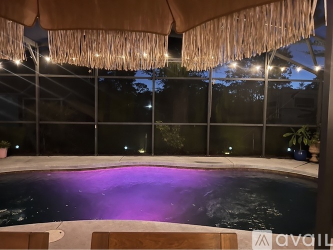 A hot tub with purple lighting under a straw umbrella.