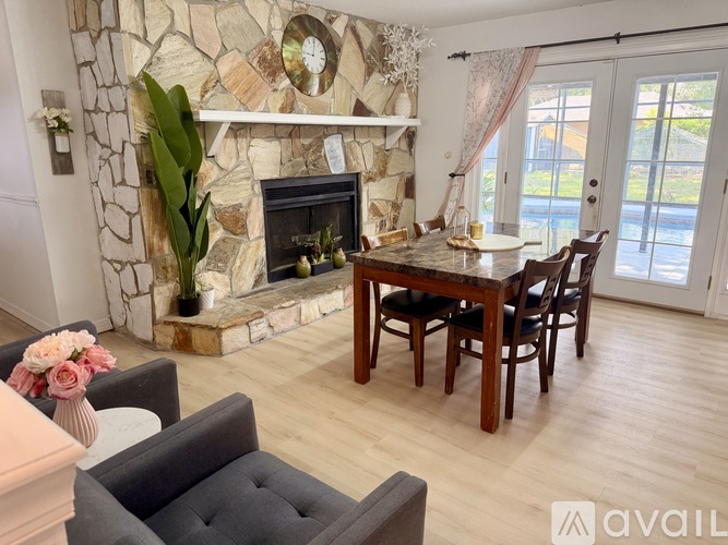 A living room with a stone fireplace and a dining table with chairs.
