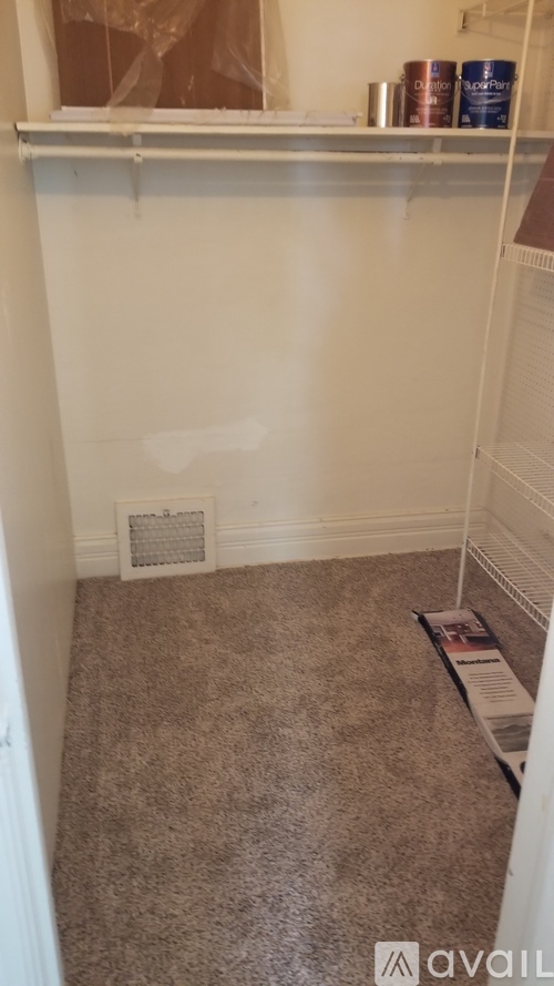 A room with a carpeted floor and a small vent on the wall.