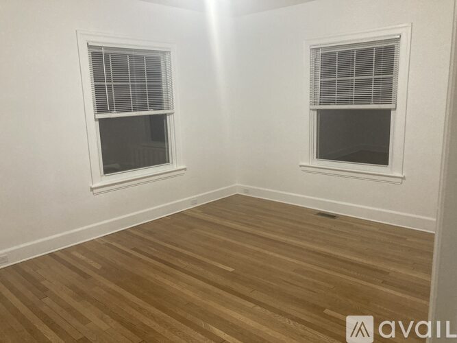 A room with wooden flooring and two windows.