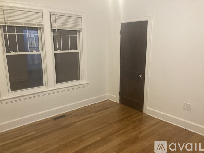 A room with wooden flooring, a window with blinds, and a closed door.