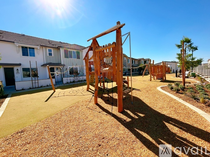 A playground with a wooden swing set in the foreground and houses in the background.
