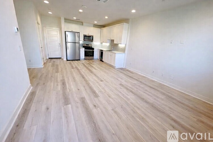 A spacious room with wooden flooring and a kitchen area with a refrigerator, microwave, and oven.