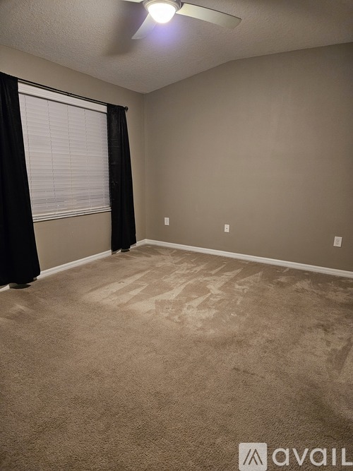 A room with a carpeted floor and a window with black curtains.