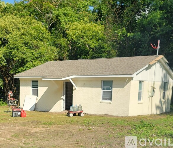 A small white house with a brown roof is surrounded by greenery.