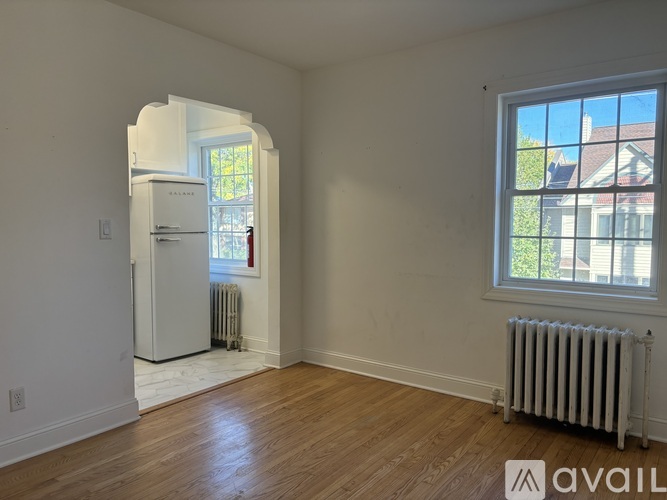A room with a white wall and a window with a view of a house across the street.