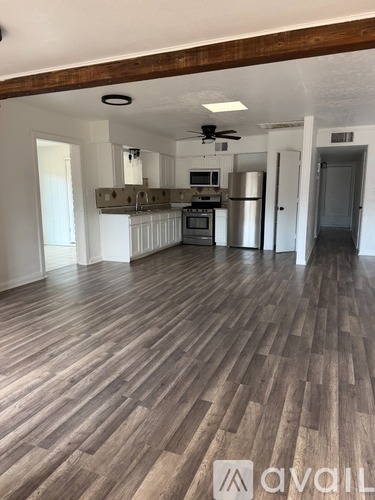 A room with wooden flooring and a kitchen area in the background.