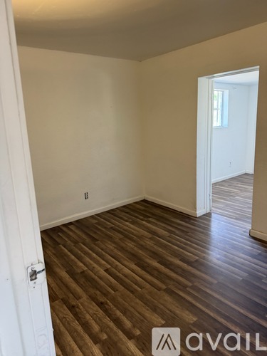 A room with wooden flooring and a door leading to another room.