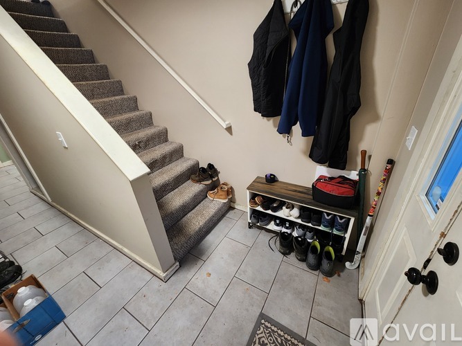 A hallway with a staircase and a bench with shoes and jackets hanging on the wall.