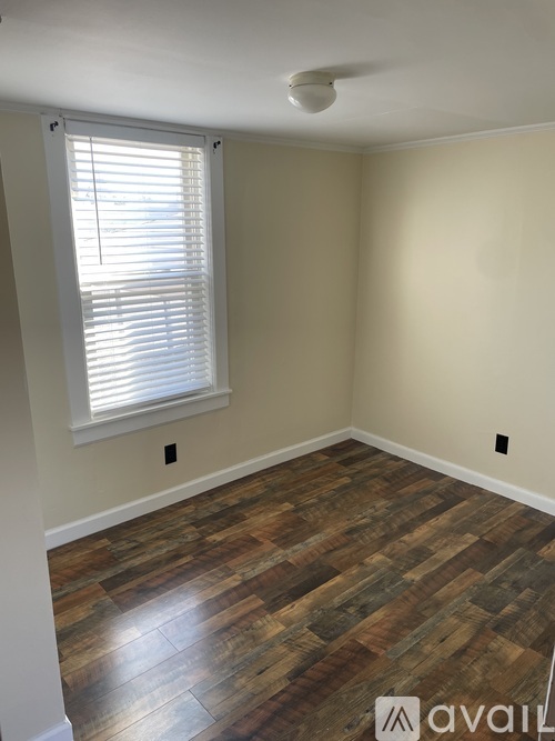 A room with wooden flooring and a window with blinds.