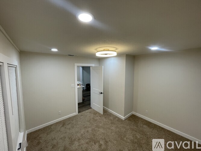 A well-lit, empty room with a carpeted floor and a doorway leading to another room.