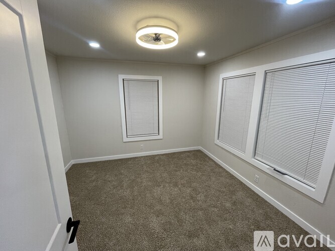 A room with a carpeted floor, a window with blinds, and a ceiling light.