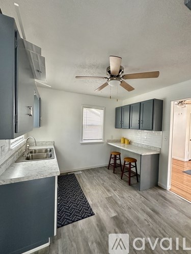 A kitchen with a fan on the ceiling and a bar area with stools.