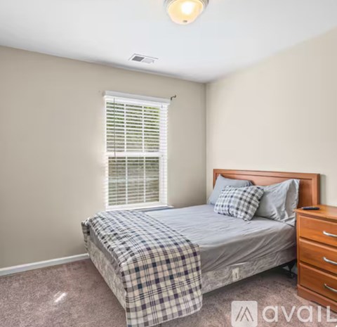 A bedroom with a bed, nightstand, and window with blinds.