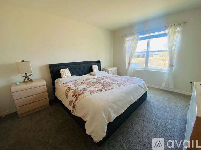 A bedroom with a large bed and a window with curtains.