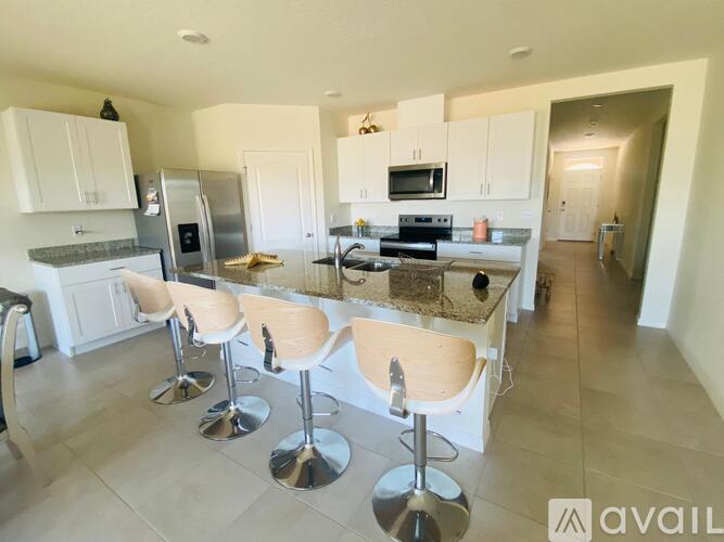 A kitchen with white cabinets and a bar area with stools.