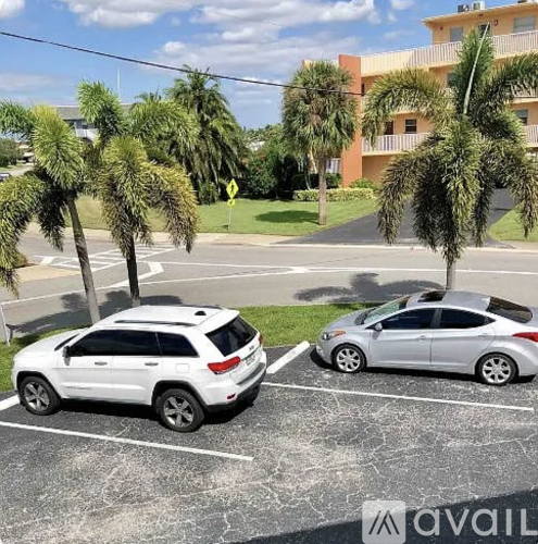 Two cars are parked in a parking lot with palm trees in the background.