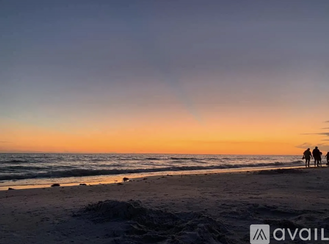 Three people are standing on a beach at sunset.