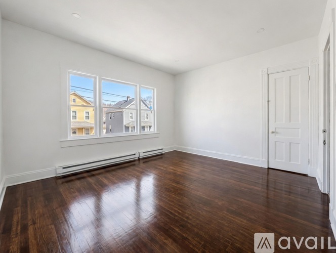 A room with wooden floors and a window showing a view of houses outside.