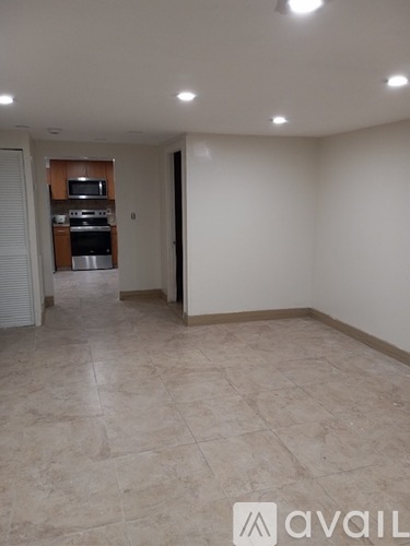 A spacious room with tiled flooring and a kitchen area in the background.