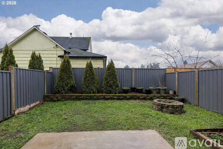 A backyard with a fence, a small tree, and a fire pit.