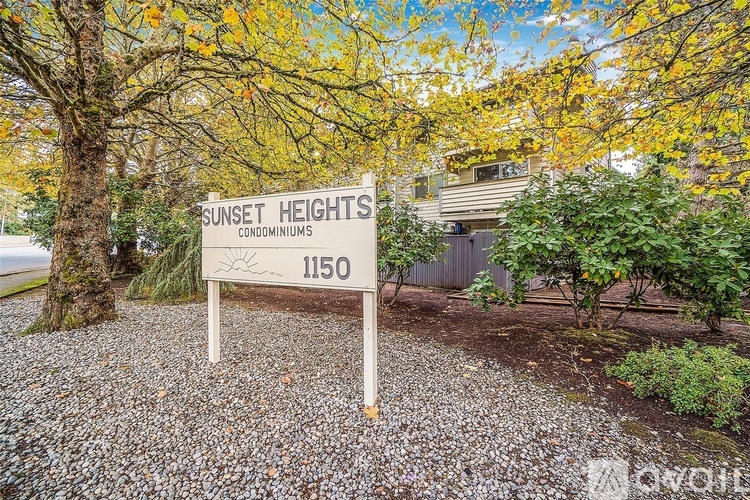 A sign for Sunset Heights Condominiums is in front of a tree with yellow leaves.